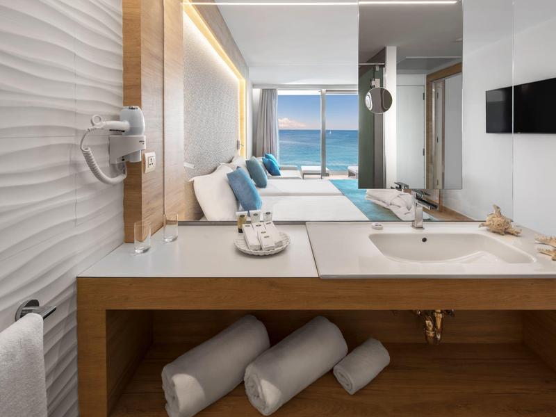 Moderní hotelový pokoj s dvojlůžkem a výhledem na moře přes velká okna.