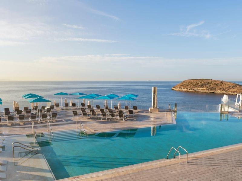 Infinity bazén u moře s lehátky a slunečníky pod jasnou oblohou