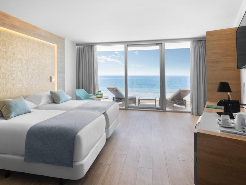 Moderní hotelový pokoj se dvěma postelemi, posezením a výhledem na moře přes velká okna