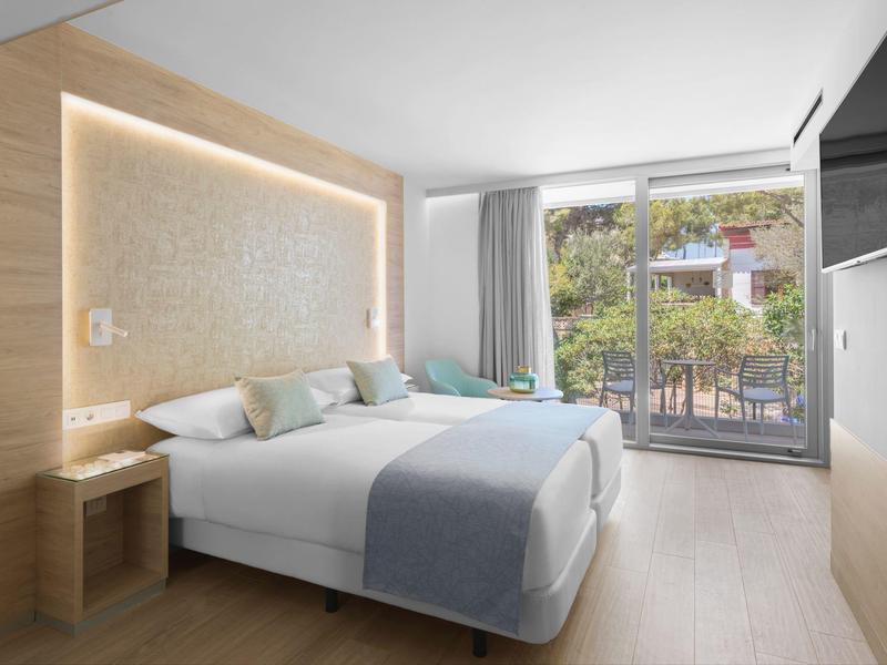 Moderní hotelový pokoj s manželskou postelí, televizí a balkonem s výhledem na zahradu