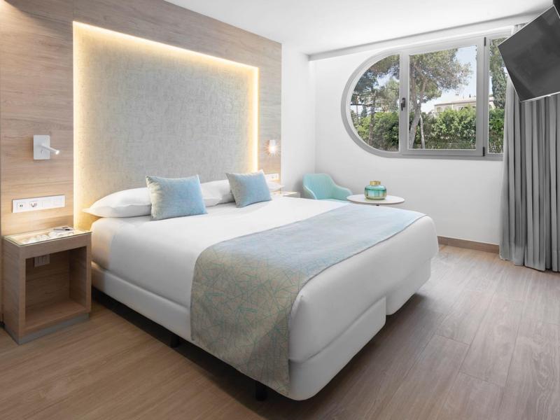 Moderní hotelový pokoj s velkou postelí, světlou dřevěnou podlahou a obloukovým oknem.