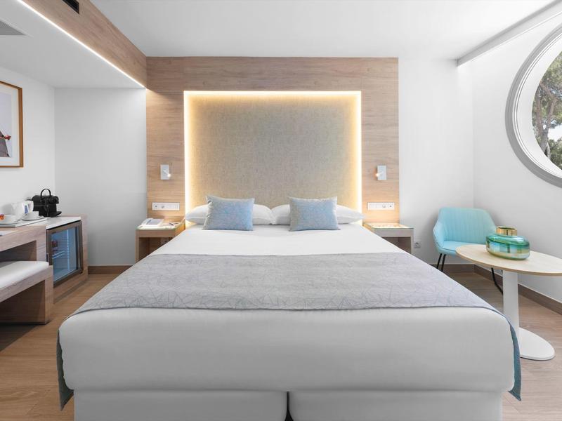 Moderní hotelový pokoj s velkou postelí, nepřímým osvětlením a posezením u okna.