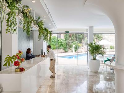 Nowoczesna lobby hotelowa z recepcją, zielonymi roślinami i widokiem na basen.