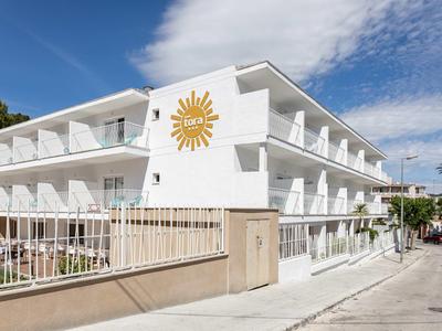 Nowoczesny biały budynek hotelowy z symbolem słońca i balkonami pod niebieskim niebem.