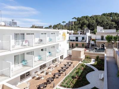 Nowoczesny kompleks hotelowy z białymi budynkami, tarasami i przestrzeniami do siedzenia na zewnątrz pod niebieskim niebem.