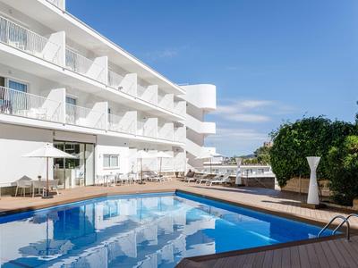 Piscina moderna dell'hotel con terrazza e balconi bianchi sotto un cielo blu chiaro.