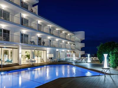 Nowoczesny hotel z oświetlonym basenem i tarasami nocą.