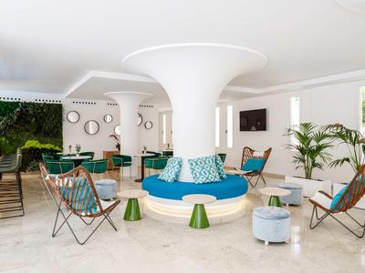 Nowoczesny hotelowy salon z okrągłymi kolumnami, kolorowymi meblami i naturalnym światłem.