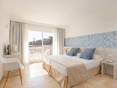 Jasny pokój hotelowy z podwójnym łóżkiem, niebieską dekoracją ściany i balkonem z widokiem.