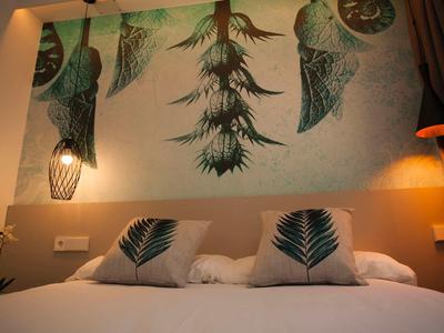 Sypialnia z łóżkiem podwójnym, ozdobnymi poduszkami i ściennym obrazem z motywem roślin tropikalnych.