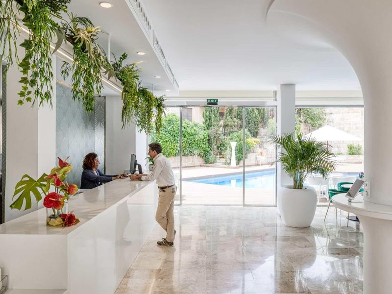 Nowoczesna lobby hotelowa z recepcją, zielonymi roślinami i widokiem na basen.