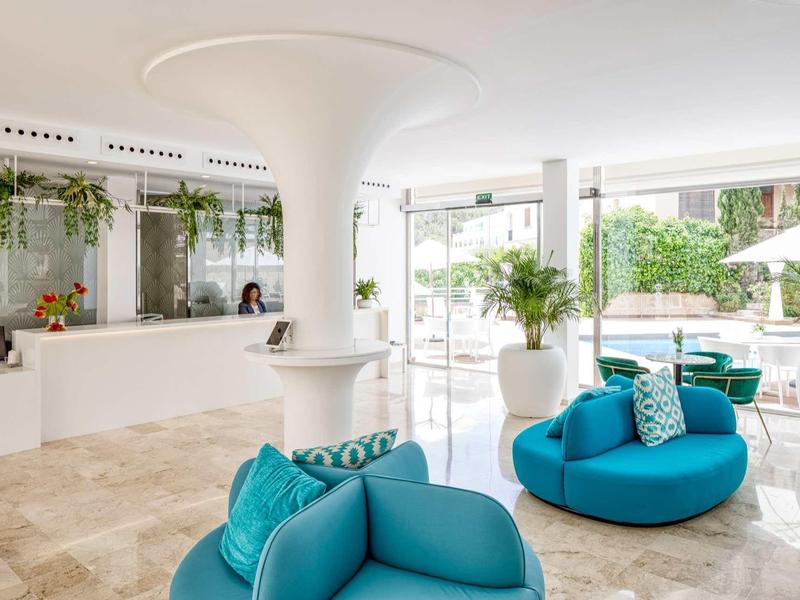 Nowoczesna przestrzeń wypoczynkowa w hotelu z niebieskimi fotelami i dużymi oknami na ogród.