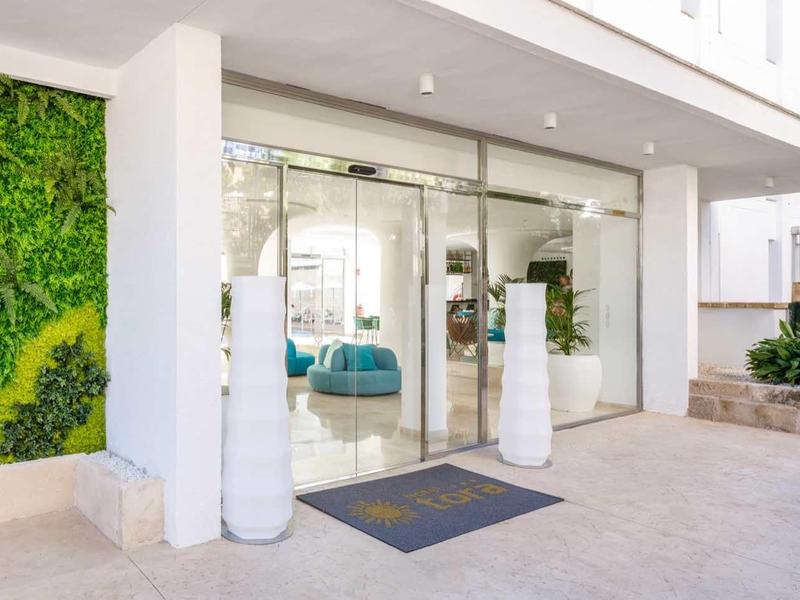 Wejście do hotelu ze szklaną elewacją, białymi kolumnami i nowoczesną zielenią na ścianie zewnętrznej.