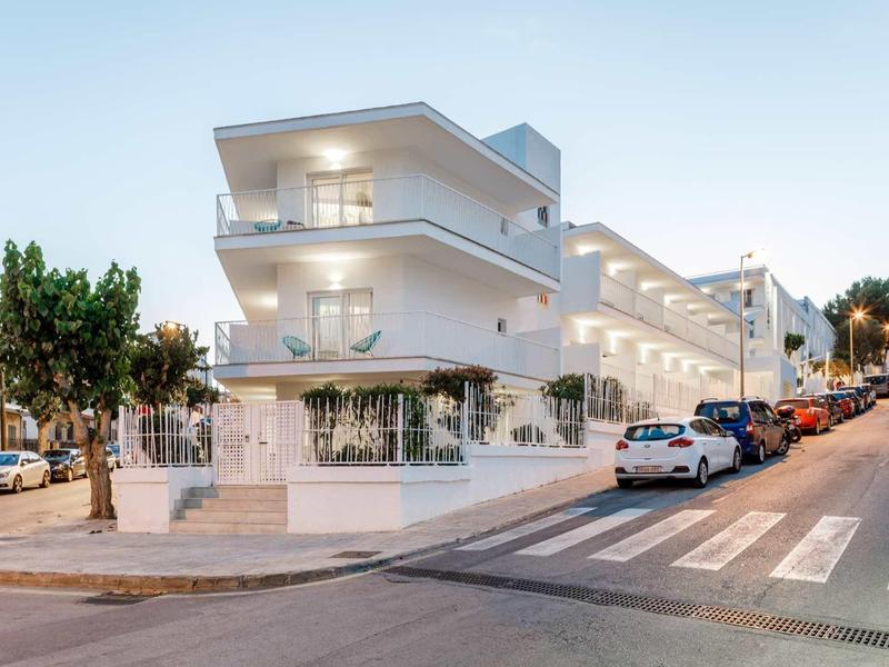 Nowoczesny biały hotel na rogu ulicy z balkonami i zaparkowanymi samochodami.