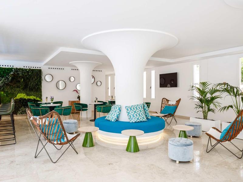 Nowoczesny hotelowy salon z okrągłymi kolumnami, kolorowymi meblami i naturalnym światłem.