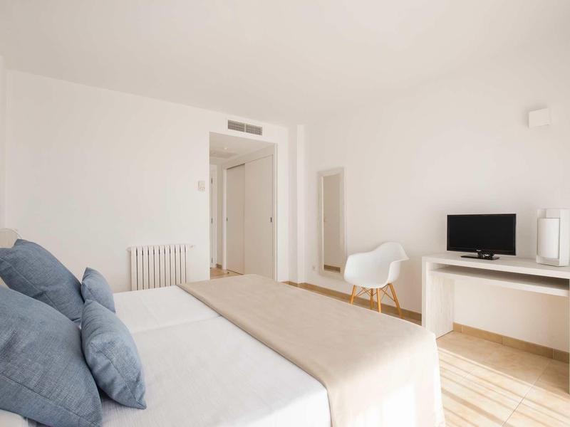 Jasny, minimalistyczny pokój hotelowy z łóżkiem, krzesłem i telewizorem.