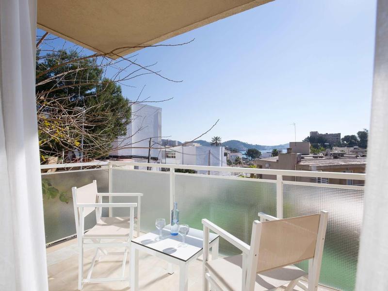 Balkon z dwoma białymi krzesłami i stołem, widok na domy i krajobraz przy czystym niebie.