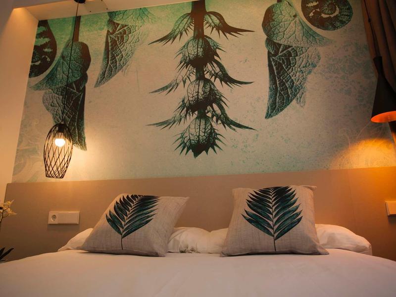Sypialnia z łóżkiem podwójnym, ozdobnymi poduszkami i ściennym obrazem z motywem roślin tropikalnych.
