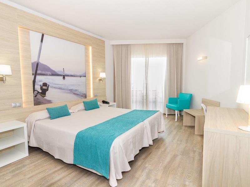 Jasno urządzone pokoje hotelowe z podwójnym łóżkiem, biurkiem, krzesłem i balkonem.