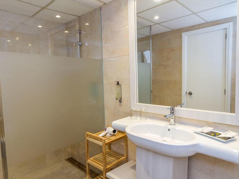 Jasna łazienka z szklaną kabiną prysznicową, dużym lustrem i umywalką z blatem.