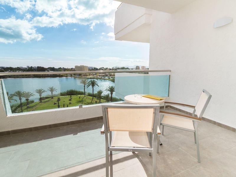 Balkon z widokiem na jezioro, taras z dwoma krzesłami i stołem w pokoju hotelowym.