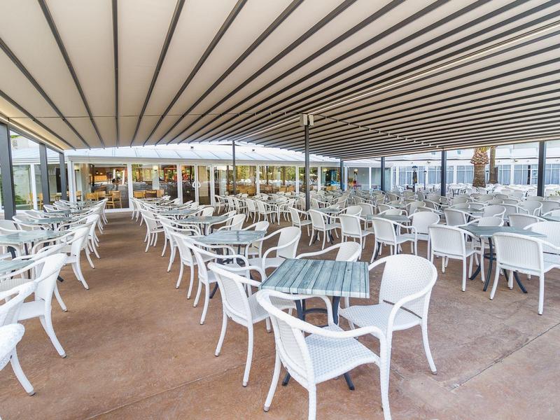 Duży zadaszony teren na zewnątrz z wieloma białymi krzesłami i stolikami w restauracji hotelowej.