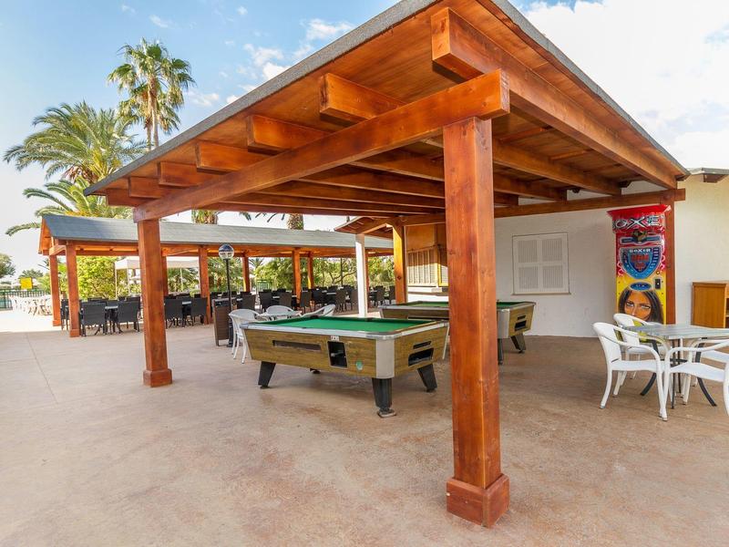 Zadaszony teren na zewnątrz z stołem do bilarda i białymi zestawami siedzeń w słonecznym hotelowym otoczeniu.