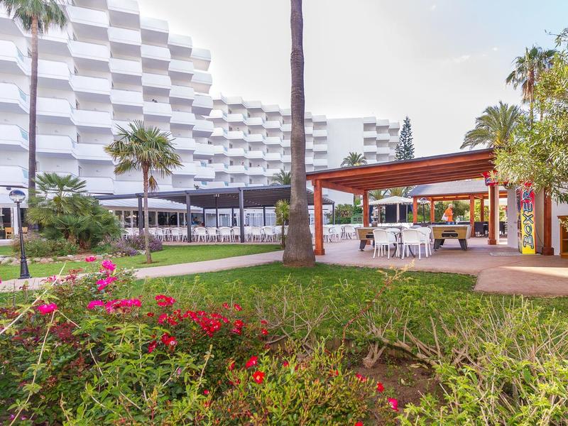 Nowoczesny kompleks hotelowy z ogrodem, palmami i zadaszonym miejscem do siedzenia w ciągu dnia.