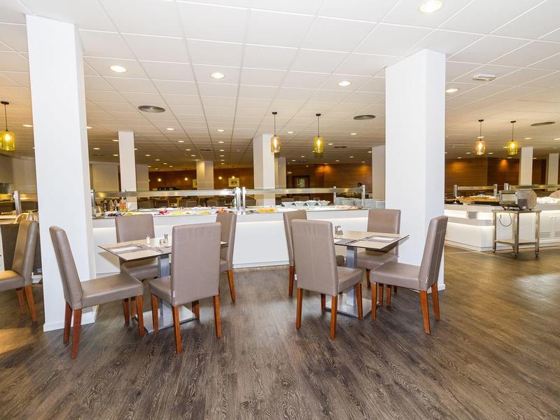 Nowoczesna, jasna restauracja z stołami i krzesłami na drewnianej podłodze.