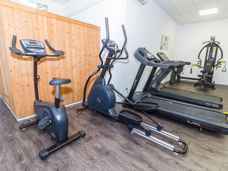 Mała siłownia z rowerkiem, orbitrekiem, bieżniami i maszyną do ćwiczeń siłowych na drewnianej podłodze.