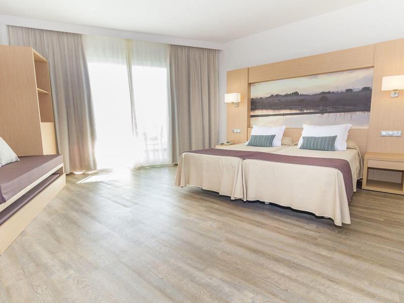 Jasny pokój hotelowy z podwójnym łóżkiem, sofą, drewnianą podłogą i dużymi oknami z zasłonami.