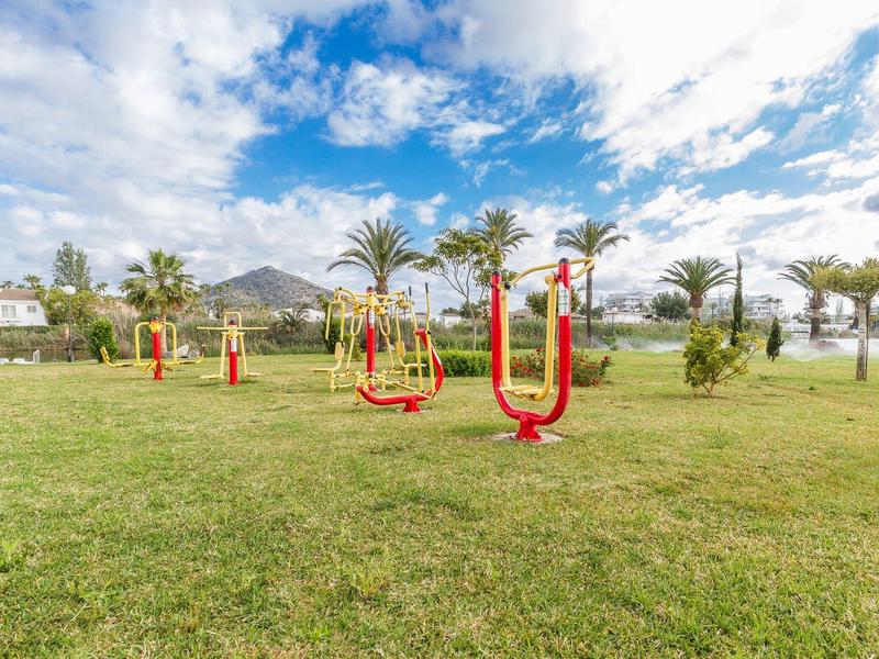 Sprzęt do ćwiczeń na świeżym powietrzu na zielonej trawie z palmami i pochmurnym niebem w tle.