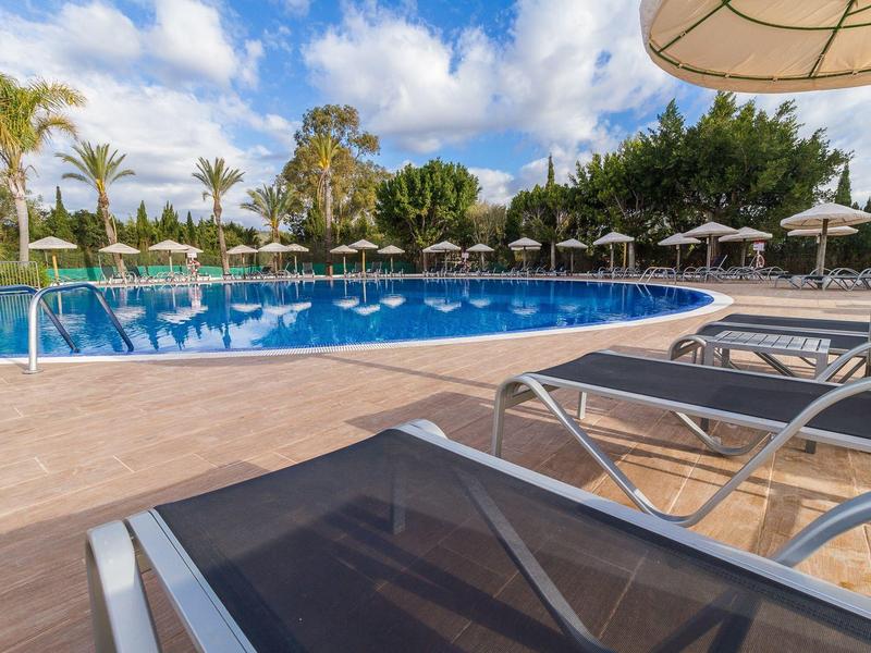 Pusta strefa basenowa z leżakami i parasolami pod niebieskim, częściowo pochmurnym niebem.