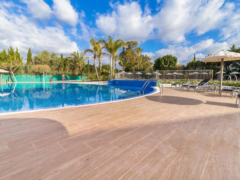 Nowoczesny basen na zewnątrz z leżakami, parasolami i palmami pod niebieskim niebem.