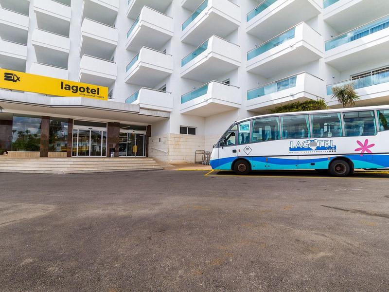 Wielopiętrowy hotel z żółtym znakiem i niebieskim busem wahadłowym przed wejściem.