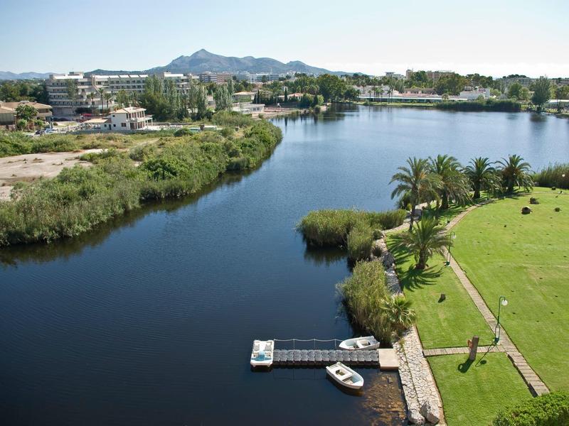 Widok na spokojne jezioro z zielonym brzegiem i pomostem pod czystym niebem.