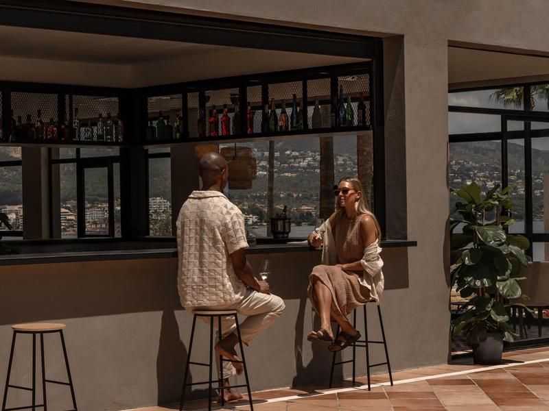 Due persone siedono a un bar con pareti di vetro con vista sulle montagne.