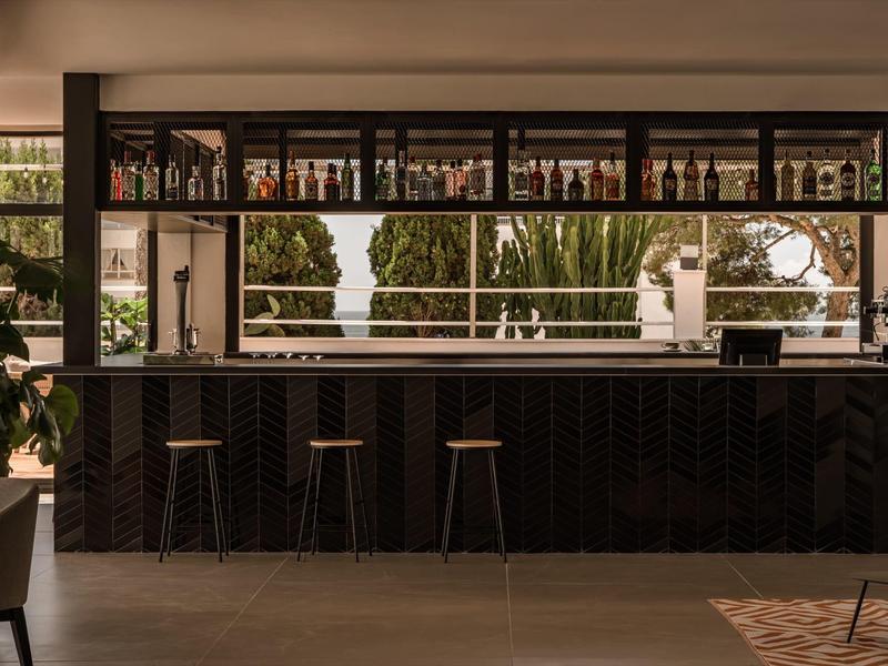 Area bar moderna dell'hotel con bancone verniciato di scuro e sgabelli davanti a grandi finestre.