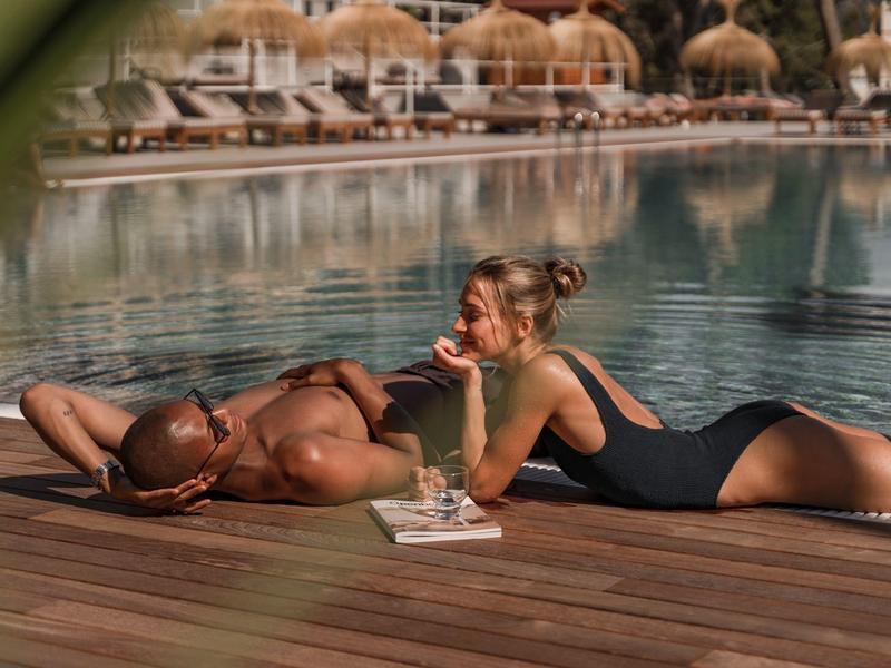 Due persone si rilassano su un ponte di legno vicino alla piscina, una legge, l'altra è distesa.