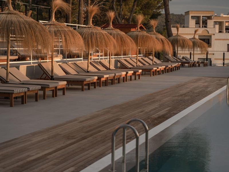 Area piscina vuota con lettini e tettoie di paglia al tramonto in un resort hotel.