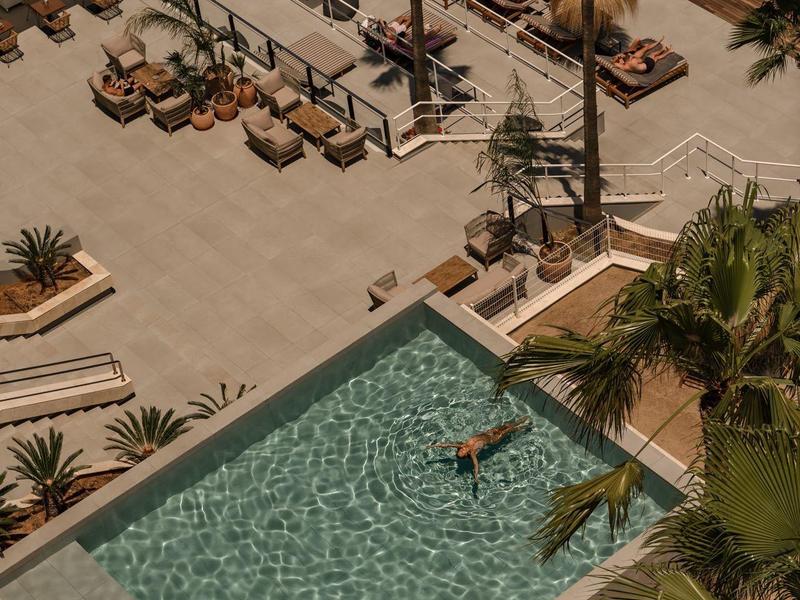 Vista di una piscina dell'hotel accanto a una piscina più grande con lettini e piante tropicali.