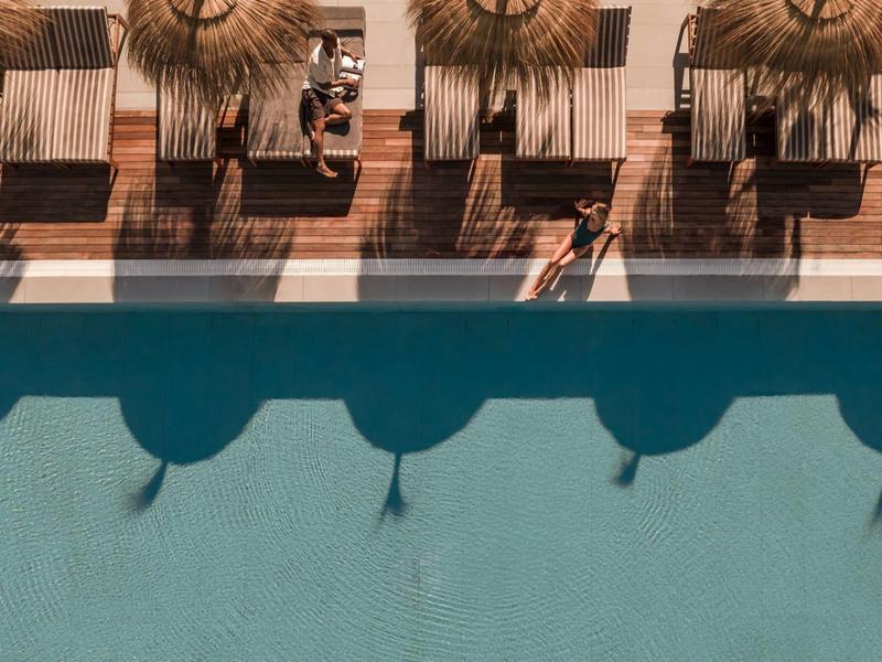 Vista sulla piscina con ombrelloni e lettini, due persone si rilassano a bordo piscina.