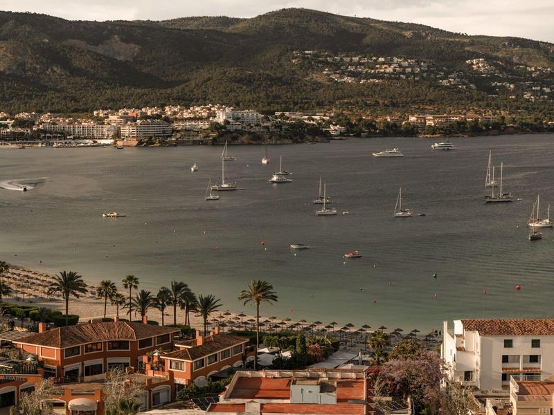 Baia con barche a vela e edifici in primo piano, circondata da colline.