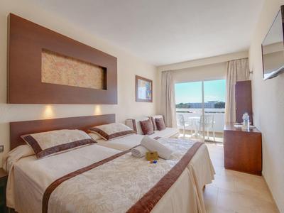 Chambre d'hôtel lumineuse avec deux lits, balcon et vue sur la mer en pleine journée.