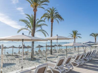 Chaises longues vides et parasols sur la plage avec des palmiers et un ciel bleu.