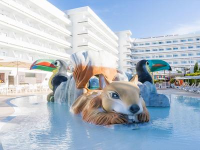 Piscine avec sculptures d'animaux colorées devant un bâtiment d'hôtel blanc sous un ciel clair