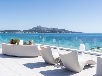 Moderne Terrasse mit weißen Liegestühlen und Pflanzen, Blick auf blaues Meer und Berge im Hintergrund.