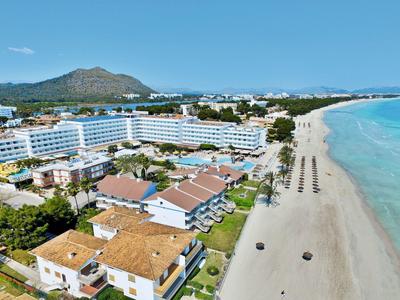 Vue aérienne d'un grand hôtel au bord de la plage avec des montagnes en arrière-plan.