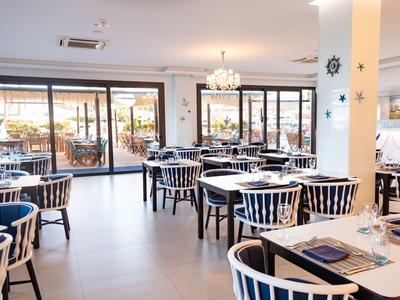 Restaurant lumineux avec des chaises blanches et bleues et de grandes fenêtres donnant sur l'extérieur.