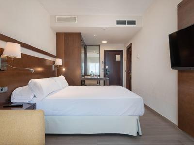 Chambre d'hôtel moderne avec grand lit, lampes murales et télévision à écran plat.